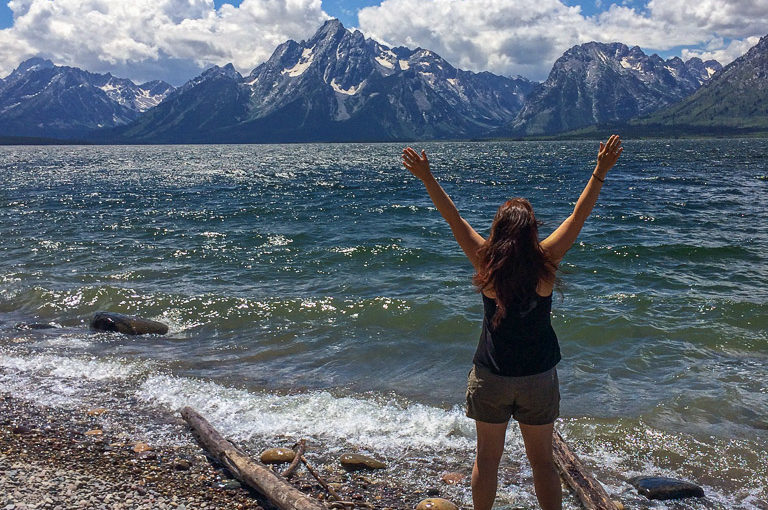 Becky raises her arms to embrace the awesomeness of the Tetons on the shore of Jackson Lake in Grand Teton National Park.