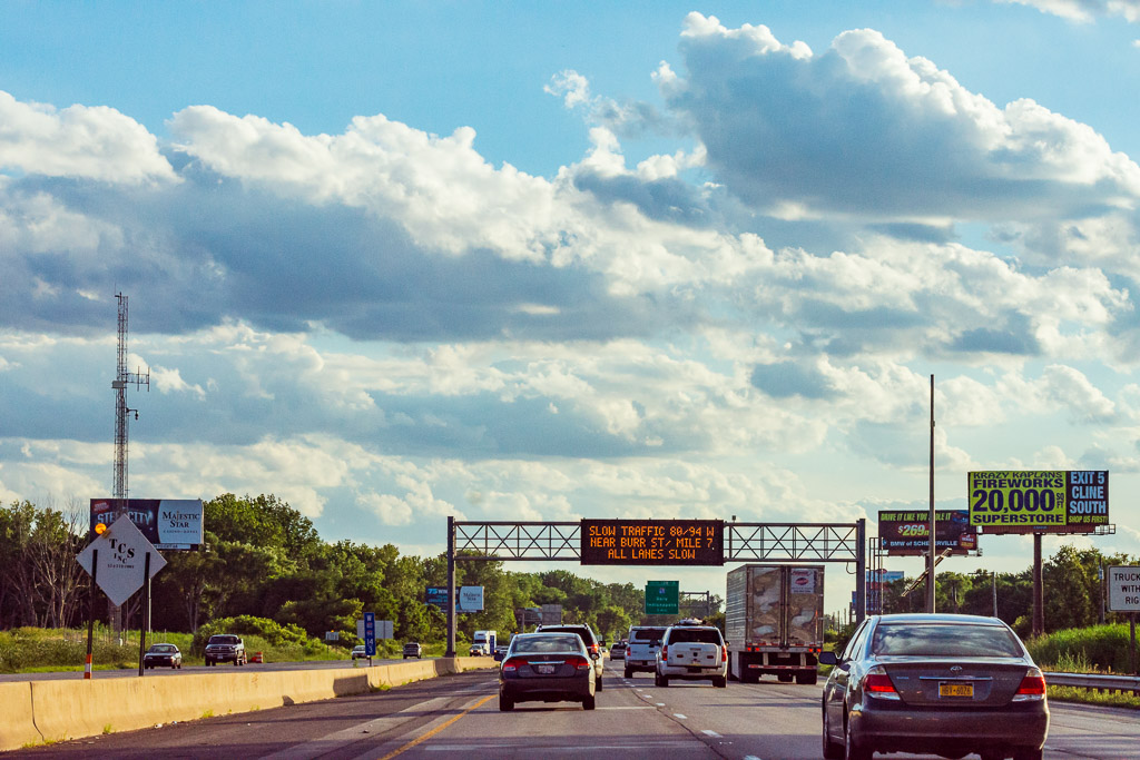 Traffic flows under partly cloudy skies on a Friday evening along I-80/94 in Lake Station, Indiana near Chicago. An electronic sign warns of slow traffic ahead.