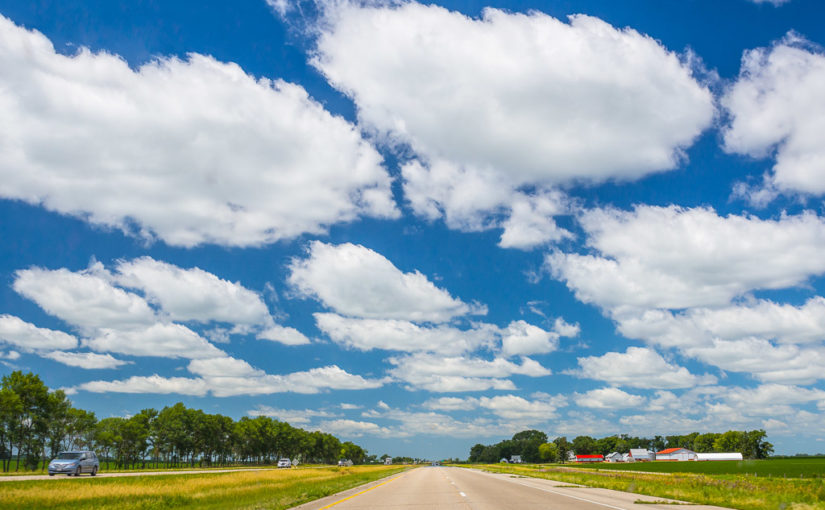 Cumulus clouds stretch across the sky over I-90 and prairie farmlands near Blue Earth, Minnesota.