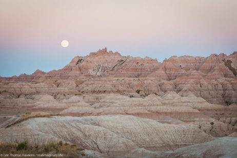 A full moon rises over The Castle at sunset from the White River Valley Overlook in Badlands National Park in South Dakota.