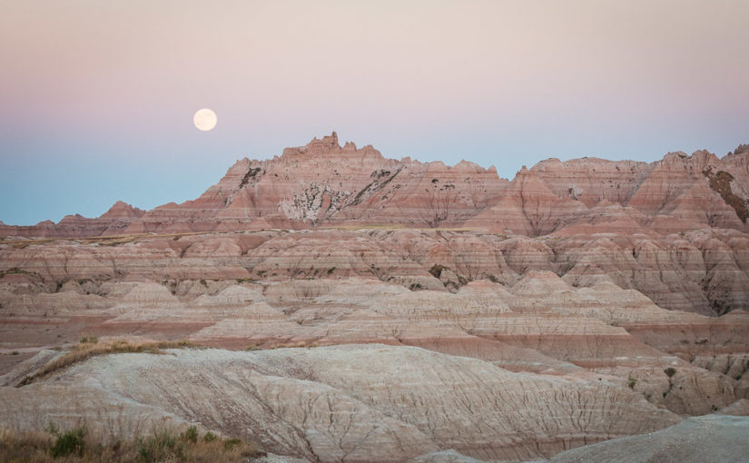 A full moon rises over The Castle at sunset from the White River Valley Overlook in Badlands National Park in South Dakota.
