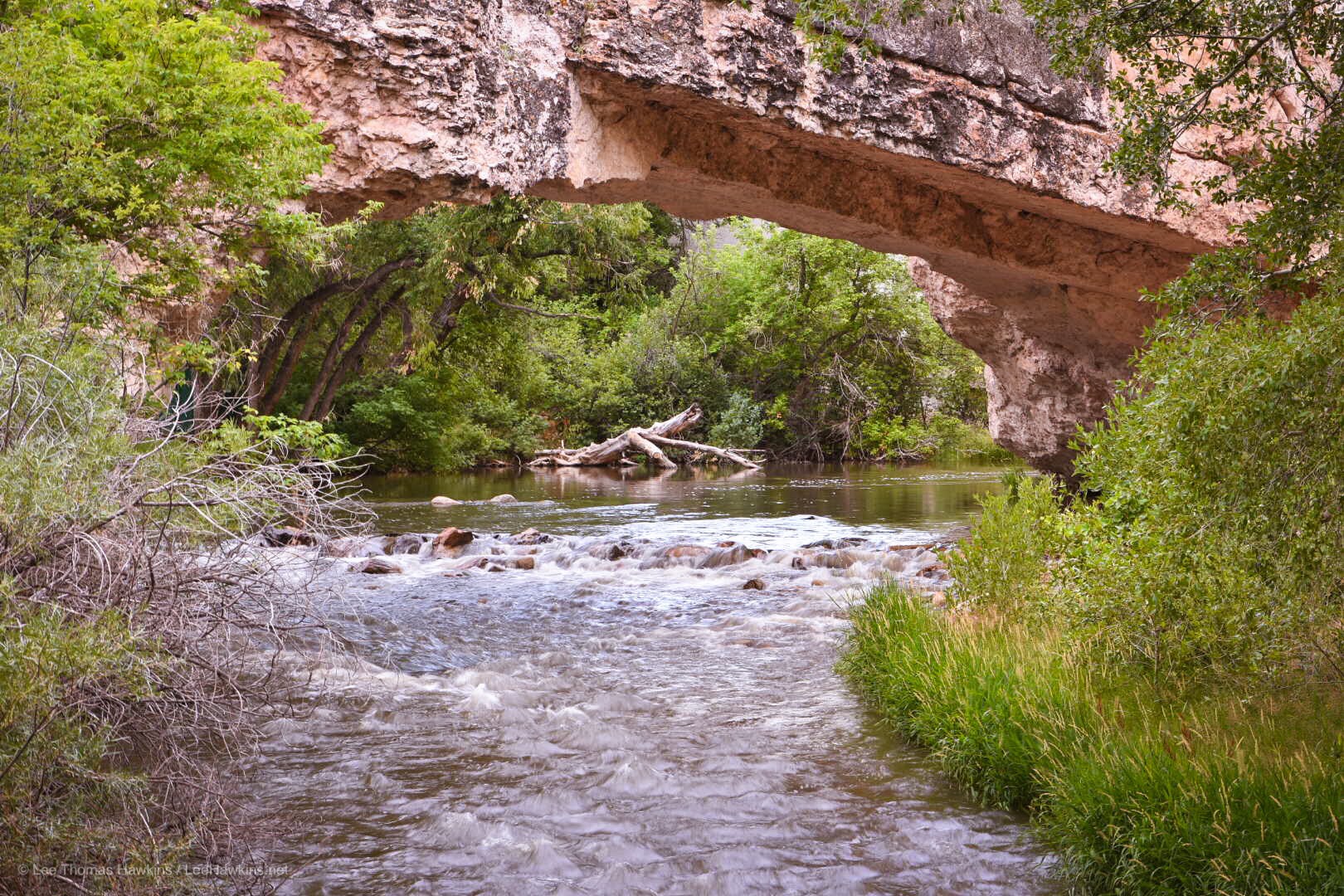 Rock extends over a river, forming a natural bridge.