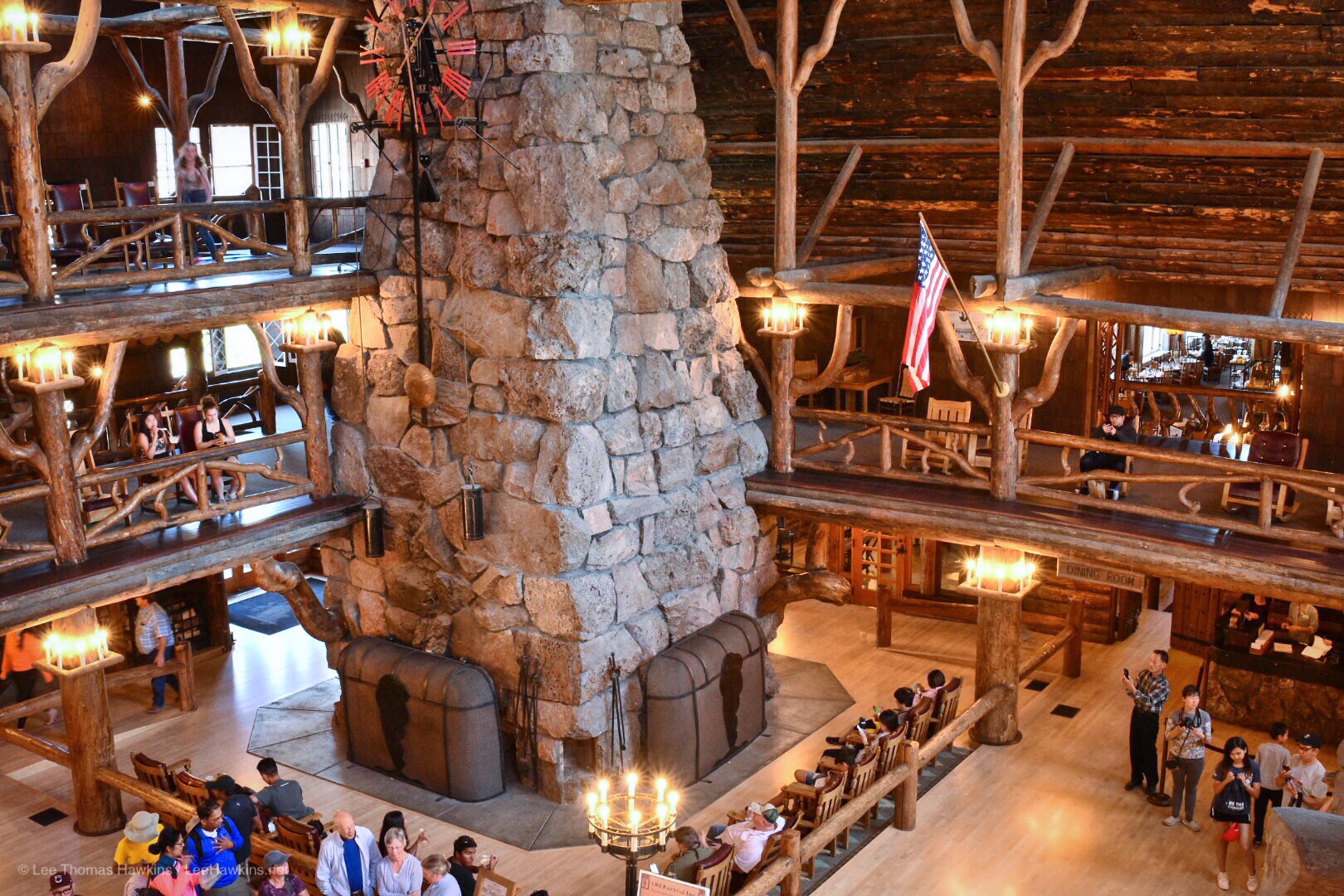 The rustic wood atrium of a hotel lobby rises multiple levels around a stone chimney surrounded by people.