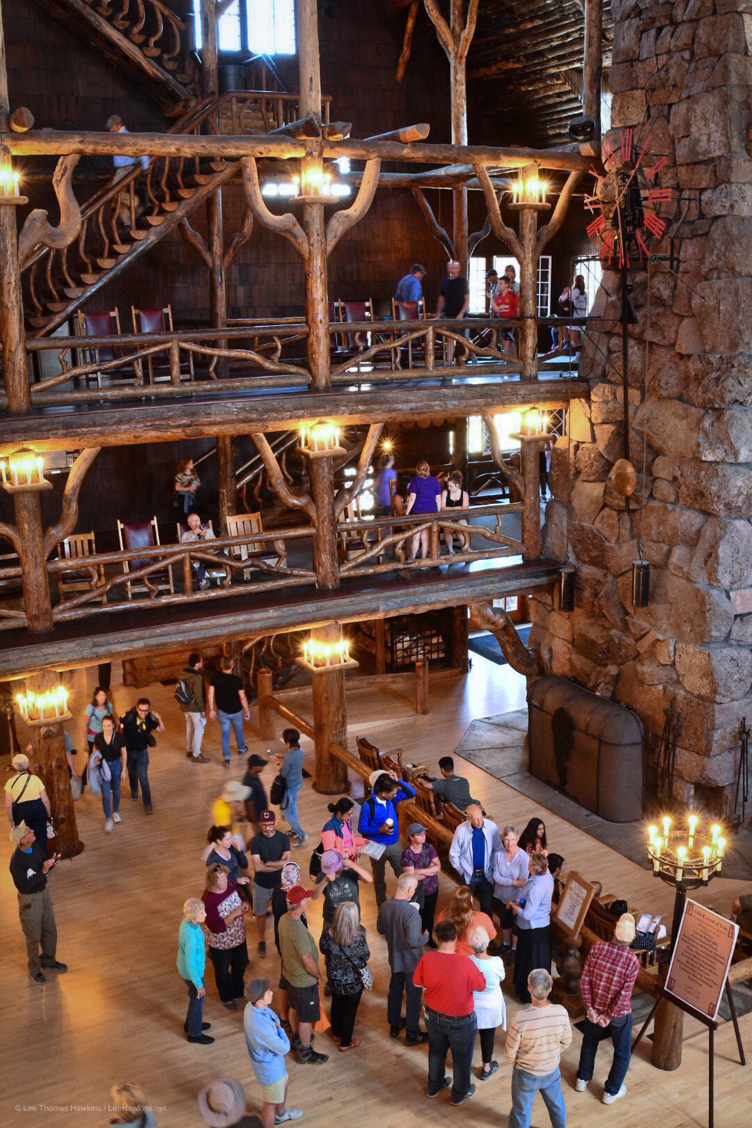 The rustic wood atrium of a hotel lobby with grand staircases rises multiple levels around a stone chimney surrounded by people.