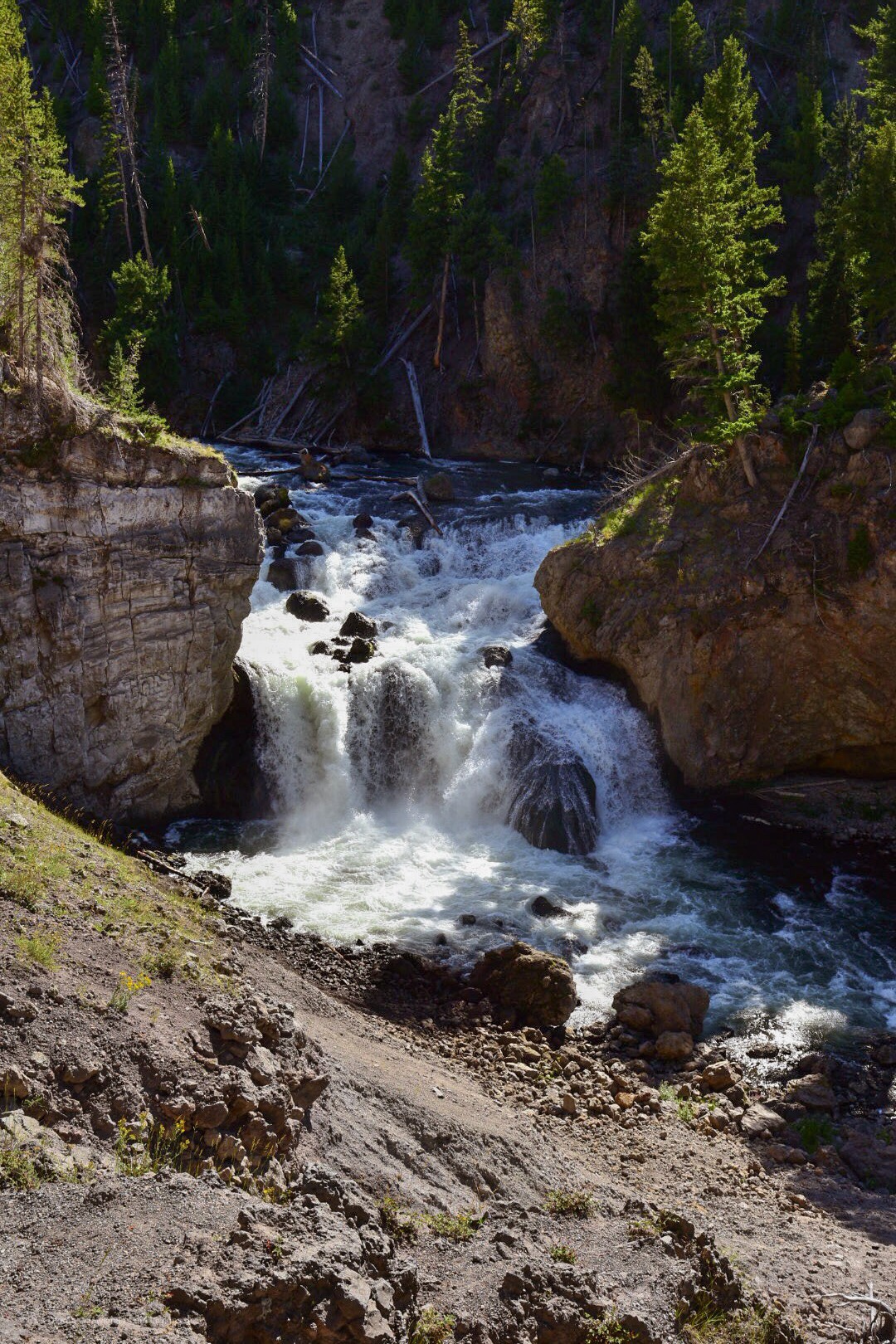 A waterfall flows through a gap in the rocks of a steep canyon.